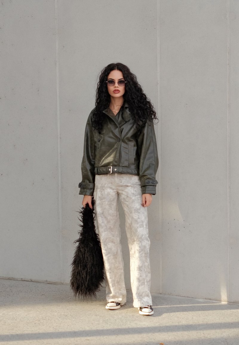 Green leather cropped jacket, light patterned trousers, and a black fluffy bag. Small round sunglasses complete the look.