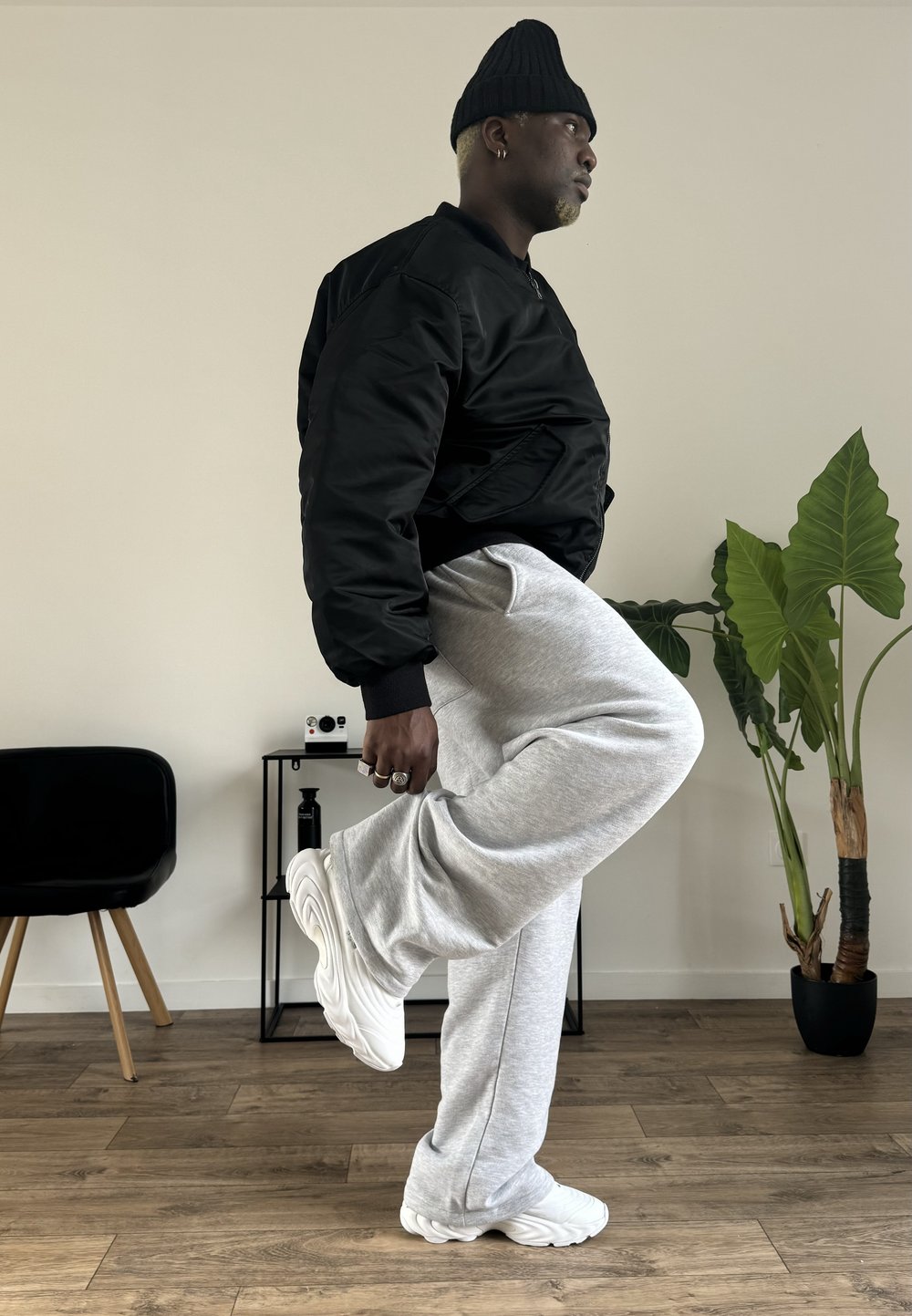 Fekete bombázó dzseki, világosszürke melegítőnadrág és fehér tornacipő. A dzseki sima tapintású; a nadrág puha, laza szabású.