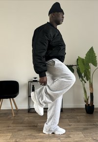 Fekete bombázó dzseki, világosszürke melegítőnadrág és fehér tornacipő. A dzseki sima tapintású; a nadrág puha, laza szabású.