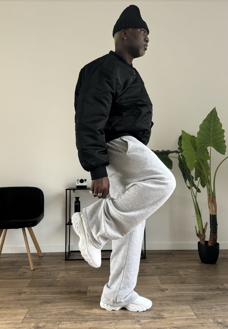 Black bomber jacket, light gray sweatpants, and white sneakers. The jacket has a smooth texture; the pants are soft, with a relaxed fit.