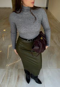 Pelēks ribots turtlenecks tops, zaļa ādas midi svārki, melns josta, bordo rokassoma un melni norādītā purngalu zābaki uz marmora grīdas.