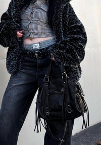 Fekete műszőrme dzseki kockás, rövid felsőn, magas derekú sötét farmerrel, szegecses övvel és bojtokkal díszített fekete bőr táskával.