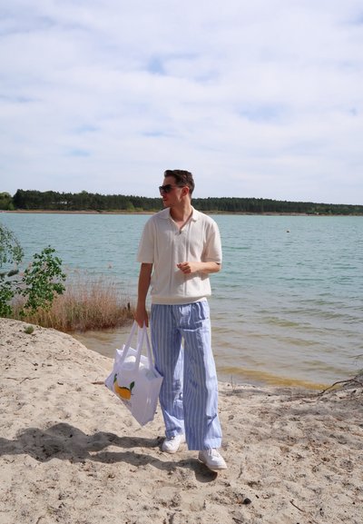 Camisa polo de color claro y manga corta, pantalones de pierna ancha a rayas azules y zapatillas blancas. Llevando una bolsa tote blanca con un diseño de limón.