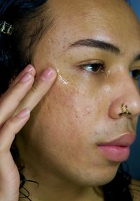 Primo piano di un volto con pelle chiara, leggero effetto luminoso da un gel, e un piercing al naso. Texture liscia con lievi imperfezioni visibili.