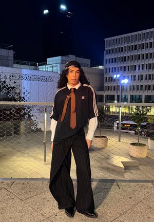 Camiseta negra de gran tamaño con rayas blancas, corbata marrón y camisa blanca debajo; pantalones de pierna ancha a rayas; zapatos negros y brillantes; entorno urbano nocturno.