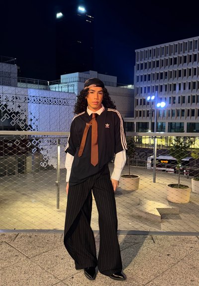 Camiseta negra de gran tamaño con rayas blancas, corbata marrón y camisa blanca debajo; pantalones de pierna ancha a rayas; zapatos negros y brillantes; entorno urbano nocturno.