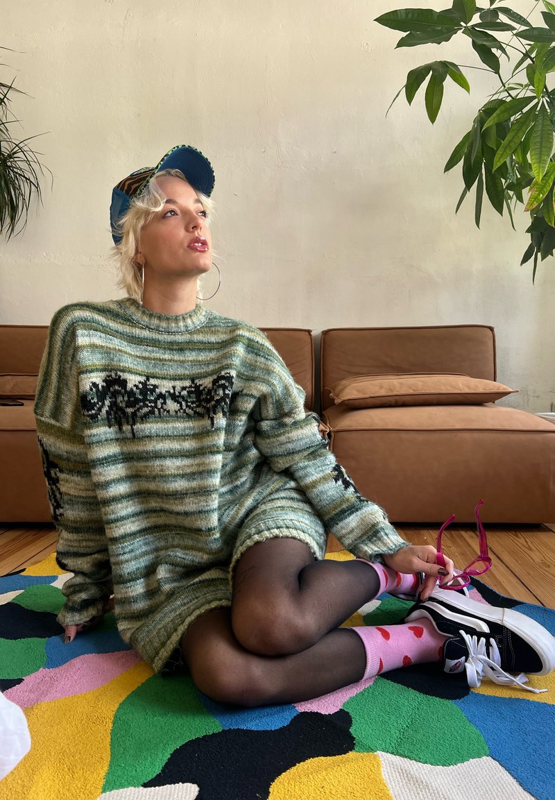 Πλεκτό oversized πουλόβερ σε πράσινες και κρεμ ρίγες, με σχέδιο μαύρων λουλουδιών. Μαύρες κολάν και ροζ καλτσάκια με βαμβακερές τελίτσες, συνδυασμένα με μαύρα sneakers.