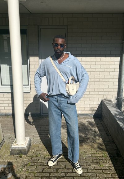 Camisa de manga larga azul claro con cuello, combinada con pantalones vaqueros de pierna ancha. Pequeño bolso blanco de hombro y zapatillas negras con suelas color crema.