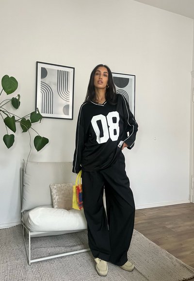Jersey negro oversize con estampado blanco "08", combinado con pantalones anchos negros. Los accesorios incluyen una bolsa de malla colorida y zapatos de lona en tonos neutros.
