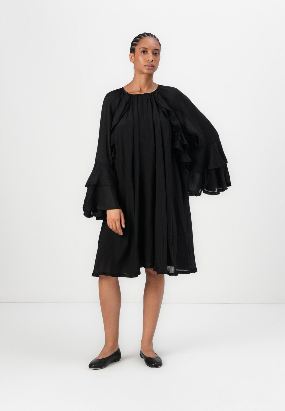 Vestito nero con maniche lunghe e volants e scollatura arricciata. Realizzato in un tessuto leggero, presenta una silhouette ampia e fluttuante.