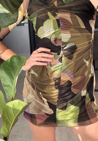 Πολυφορεμένο μίνι φόρεμα σε διάφανο, ελαφρύ ύφασμα με μοτίβο καμουφλάζ σε πράσινα, καφέ και μωβ χρώματα. Καλυμμένη εφαρμογή με κοντά μανίκια.