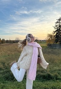 Off-white kabelstickad tröja, pastellrosa scarf, vita texturerade byxor och ljusbruna ankelboots. Accessoarer inkluderar fluffiga öronskydd.