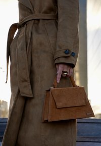 Kleine gestructureerde handtas in bruin suède met een handvat bovenaan. Voorzien van een klepsluiting en een metalen logo-accent aan de voorkant.