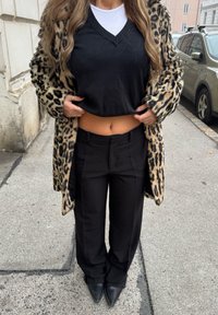 Leopardmönstrad pälsrock, svart kort topp, svarta plisserade byxor och spetsiga svarta klackar. Fokus på texturer och kontrasterande mönster.