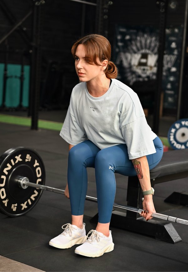 Femme en tenue de sport soulevant une barre assise sur un banc avec une expression concentrée.