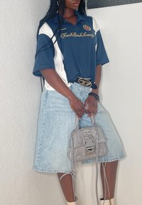 Marineblaues und weißes Poloshirt mit Logo, kombiniert mit einem hellblauen Jeansrock. Die Accessoires umfassen eine graue Handtasche mit strukturierten Details und einen Gürtel.