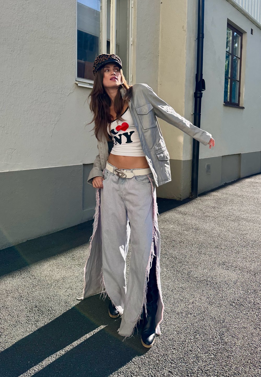 Silverfärgad jacka, vit crop top med röd/svart tryck, ljusgrå vida jeans med fransar och svarta ankelstövlar. Keps med leopardmönster.