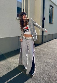 Silverfärgad jacka, vit crop top med röd/svart tryck, ljusgrå vida jeans med fransar och svarta ankelstövlar. Keps med leopardmönster.