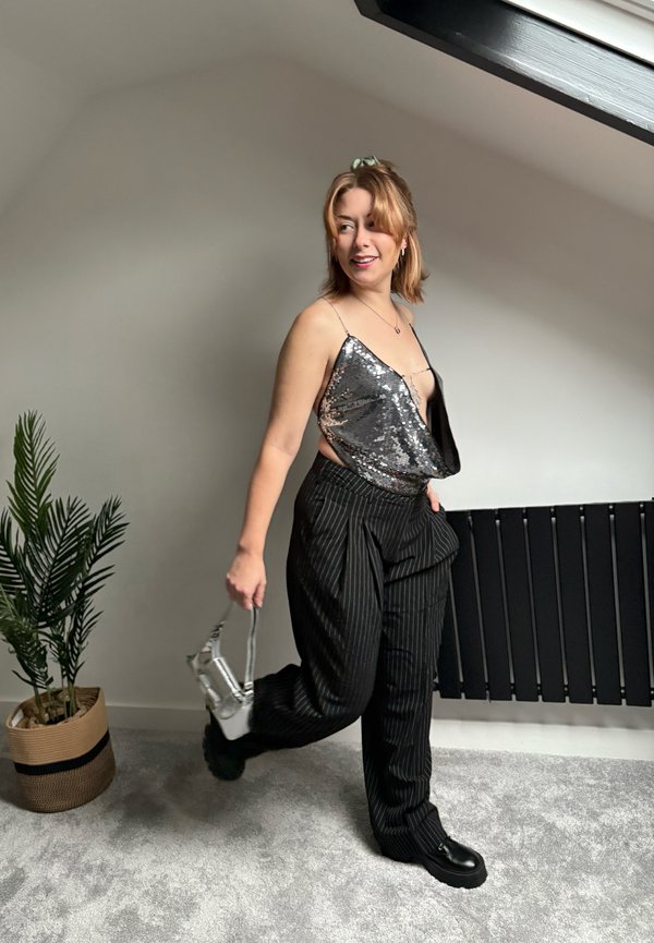 Spīguļots, bez piedurknēm tops sudraba toņos kopā ar melnām platām biksēm ar svītrainu rakstu. Aksesuārs ir mazs sudraba rokassomiņa.