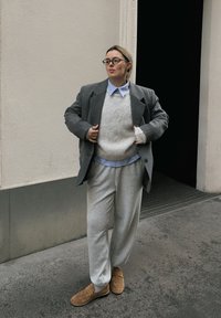 Grå oversized blazer, kremfarget genser i strikk over lyseblå skjorte med krage, grå joggebukser og brune loafers. Glatte teksturer, avslappet passform.