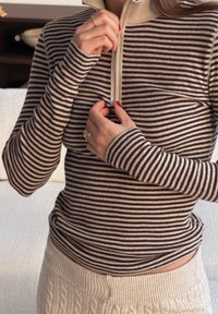 Langärmeliges, braun-cremefarben gestreiftes Oberteil mit Reißverschluss, hohem Kragen und figurbetontem Schnitt mit Daumenlöchern an den Ärmelbündchen.