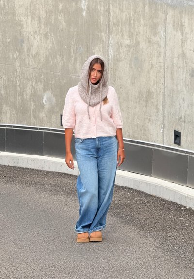 Cárdigan corto de manga corta, texturizado y rosa claro con botones; jeans de mezclilla azules holgados; bufanda de lana gris; zapatos planos color beige; fondo neutro.