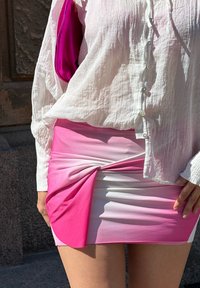 Gonna corta rosa con gradazione da chiaro a scuro, caratterizzata da un design attorcigliato sul fronte; abbinata a una camicia bianca a bottoni con texture.