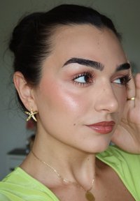 Pendientes de estrella de mar dorados, un delicado collar dorado, maquillaje natural con labios brillantes y una blusa verde se presentan en un retrato en primer plano.