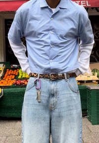 Chemise à rayures bleu clair à manches courtes sur une chemise blanche à manches longues, accompagnée d'un jean en denim bleu délavé et d'une ceinture à motif léopard.