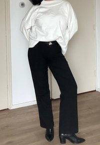 Pull blanc surdimensionné avec manches larges, associé à un pantalon noir ajusté et des talons pointus noirs. Design simple et palette de couleurs neutres.