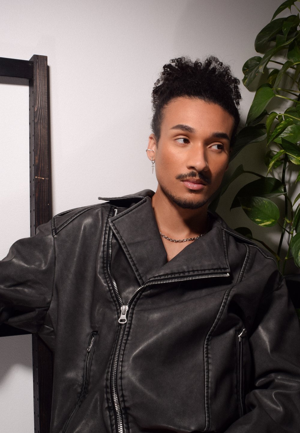 Veste en simili cuir noir avec un large col et une fermeture à glissière asymétrique, dotée d'une poche et de détails de couture. Chaîne en argent visible.