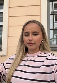 Sweatshirt i lyserød med mørkebrune vandrette striber. Har rund hals og ribbede ærmegab. Bærer en grøn halskæde og guldringe.