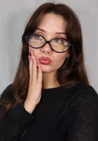 Gafas con lentes transparentes y de tono púrpura, montura negra redonda, usadas con cabello largo castaño y una camiseta negra de manga larga.