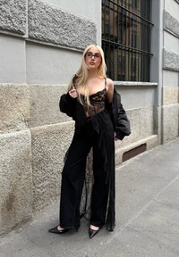 Czarny koronkowy bodysuit założony pod długą, czarną przezroczystą kurtkę, w połączeniu z czarnymi, wysokogatunkowymi dżinsami o wysokim stanie i czarnymi, spiczastymi szpilkami.