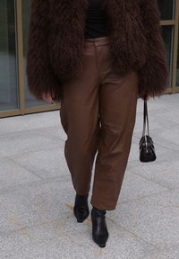 Pantaloni in pelle marrone con vestibilità ampia, abbinati a stivaletti neri con punta e una piccola borsa nera. Il capo esterno è realizzato in materiale marrone soffice.