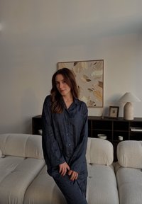 Satenast komplet pižame v mornarsko modri barvi z zgornjim delom na gumbe s ovratnikom in subtilnim cvetličnim vzorcem, v kombinaciji z ujemajočimi se hlačami. Mehka tekstura.