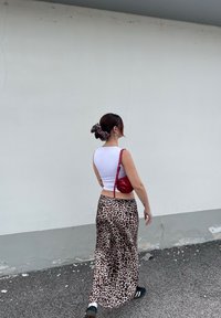 Rote Handtasche, weißes, tailliertes Crop-Top und ein langer Rock im Leopardenmuster. Haare mit einem gemusterten Haargummi gebunden. Schwarze Sandalen.