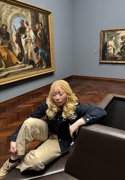 Asientos de cuero marrón con una superficie texturizada, rodeados de pinturas ornamentadas. El fondo presenta paredes de color gris claro y un suelo de madera.