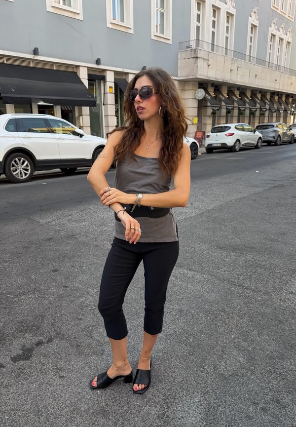Femme aux longs cheveux portant des lunettes de soleil ajustant des bracelets, debout dans une rue de la ville avec des voitures en stationnement et des bâtiments en arrière-plan.