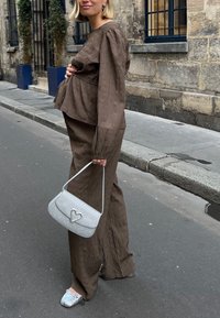 Brun, strukturerad tvådelad outfit med långärmar, matchad med en silverhandväska med hjärtdetalj och ljusblå mönstrade skor.