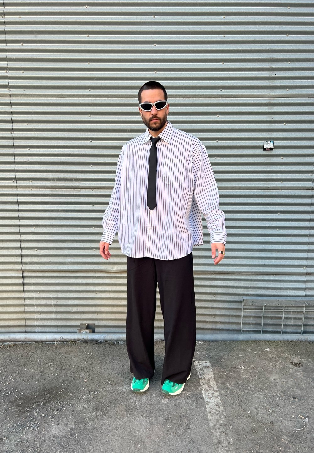 Ριγέ υπερμεγέθη λευκό πουκάμισο, μαύρο παντελόνι, μαύρη γραβάτα και πράσινα αθλητικά παπούτσια. Τα αξεσουάρ περιλαμβάνουν λευκά γυαλιά ηλίου και ασημένια κοσμήματα.