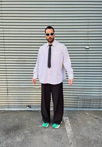 Ριγέ υπερμεγέθη λευκό πουκάμισο, μαύρο παντελόνι, μαύρη γραβάτα και πράσινα αθλητικά παπούτσια. Τα αξεσουάρ περιλαμβάνουν λευκά γυαλιά ηλίου και ασημένια κοσμήματα.