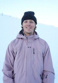 Pink waterproof jacket with zippers, featuring a high collar and hood. Black knit beanie. Snowy background.