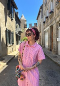 Vestido camisola riscado, em rosa e branco, com mangas curtas, dois bolsos e um corte descontraído. Os acessórios incluem uma bolsa estampada e óculos de sol.