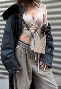 Femme portant un haut cache-cœur rose clair, une veste en cuir noire oversize, un pantalon large à carreaux, et portant un sac à main beige à motifs en bandoulière.
