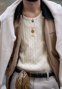 Beige gestrickter Pullover mit Lochmuster, unter einer hellbraunen Jacke getragen. Goldene Ketten und ein brauner Bandana-Sakkoeinsatz.
