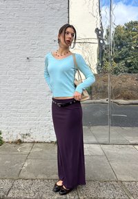 Lysblå sweater med v-udskæring, lange ærmer; lilla maxiskirt med et sort bælte; sorte ballerinaer; lille beige skuldertaske.