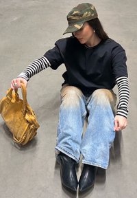 T-shirt noire superposée sur un manches longues rayé noir et blanc, jean en denim bleu clair, bottines pointues noires, et un sac à main beige.