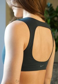 Crop top de sport gris foncé avec une large découpe dans le dos, présentant une texture lisse et un petit logo Nike sur la bande inférieure.