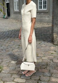 Abito a maniche corte color crema con chiusura a bottoni e texture liscia. Abbinato a una piccola borsa bianca e sandali con lacci.